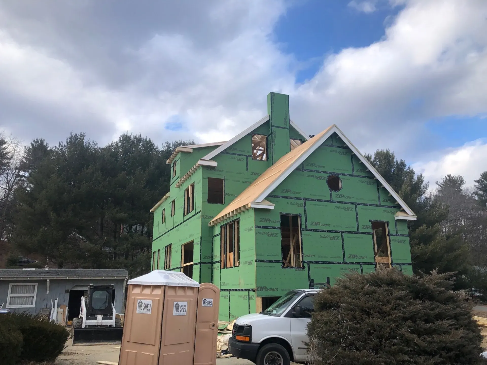 A white van is parked in front of a green house under construction.