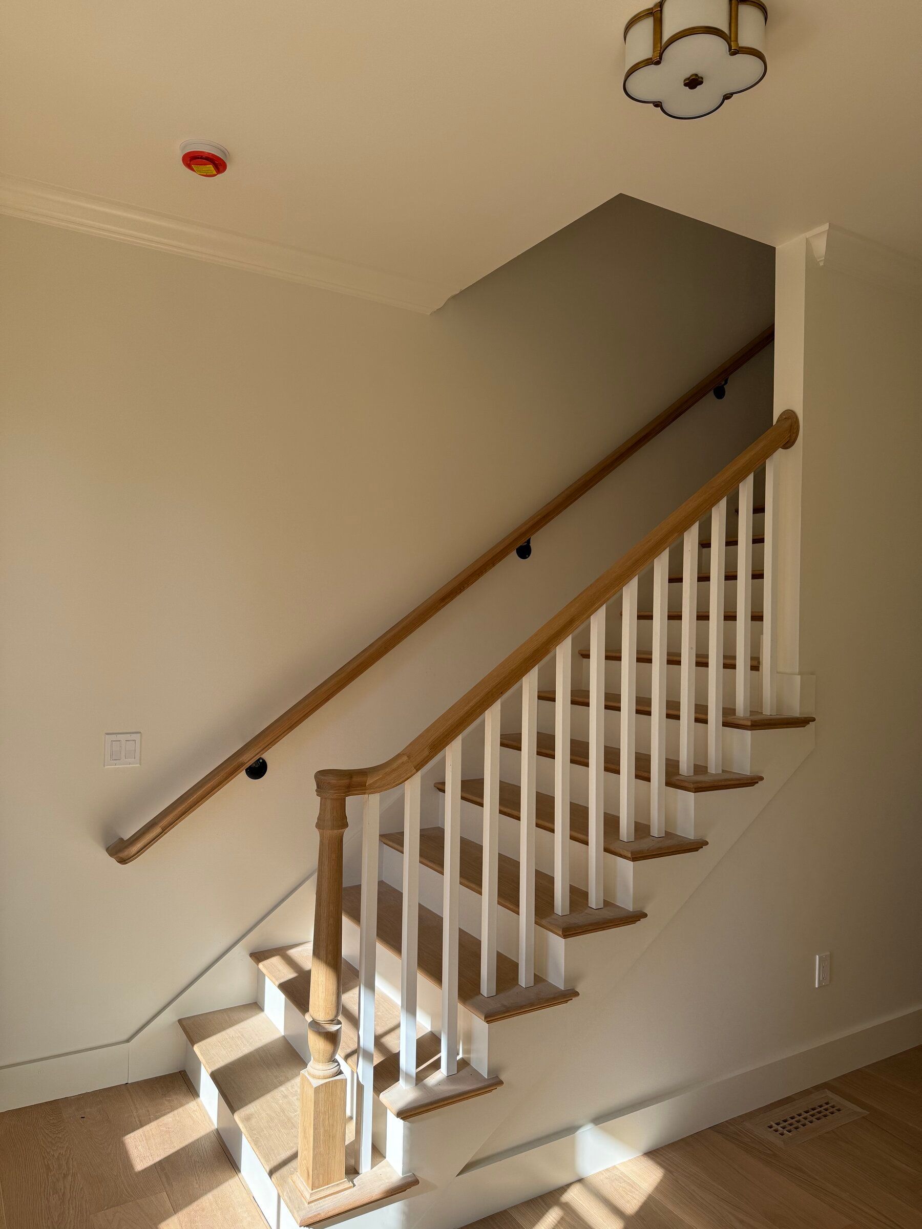 Staircase with white spindles, wooden handrail, and sunlight on beige walls in a home interior in Kittery, ME