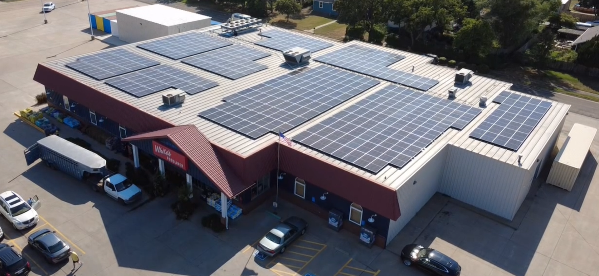 A row of solar panels against a cloudy sky with the sun shining through them.