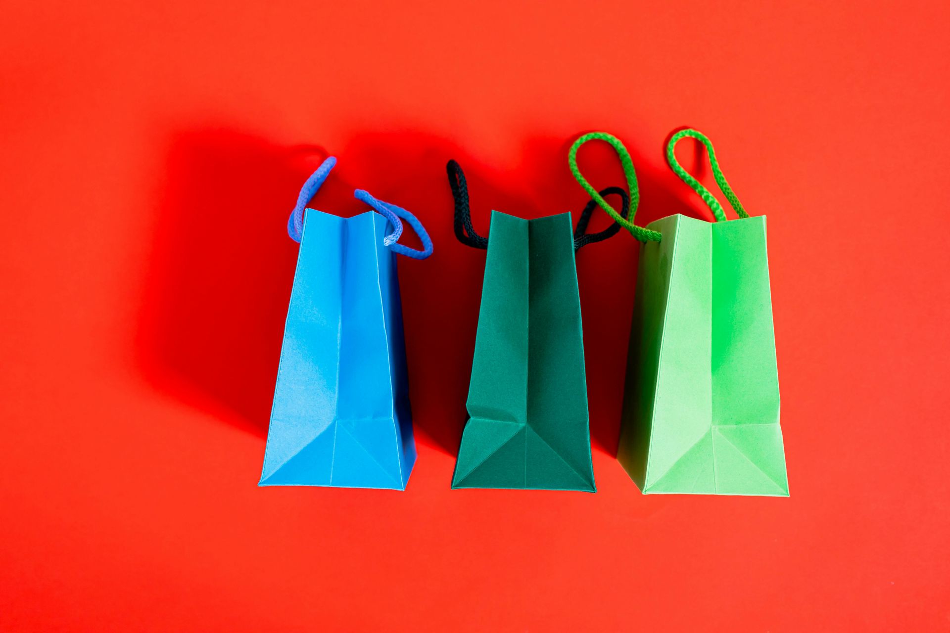 Three small gift bags: blue, dark green, and light green against a red background.