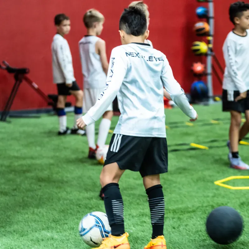 A boy wearing a shirt that says next level is kicking a soccer ball