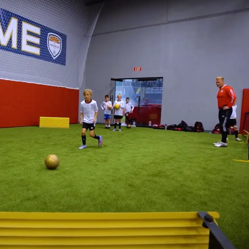 A group of kids are playing soccer in a gym with a sign above them that says