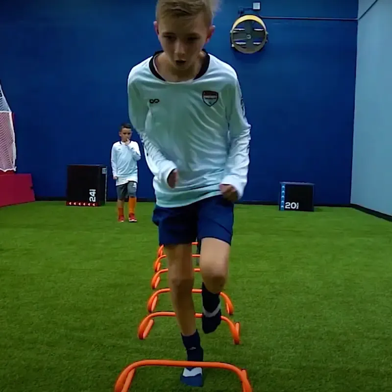 A young boy is jumping over hurdles in a gym.