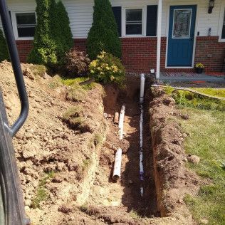 Trench dug in front yard with buried pipes running towards a house with a blue door.