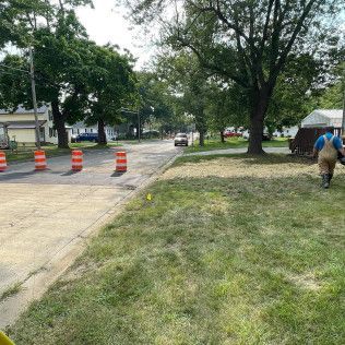 Street scene with construction barrels, a worker, and a car driving by.