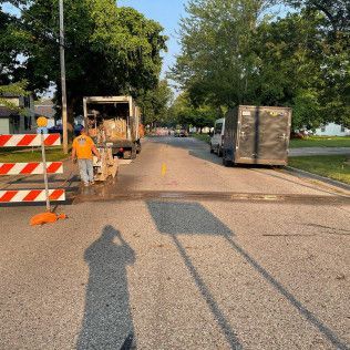 Road construction: worker, barricades, garbage truck and dump truck on street.