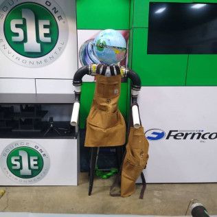 A homemade robot sculpture made of pipes, a globe head, and tool aprons in a workshop setting.