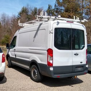 White work van with ladder rack parked outside.