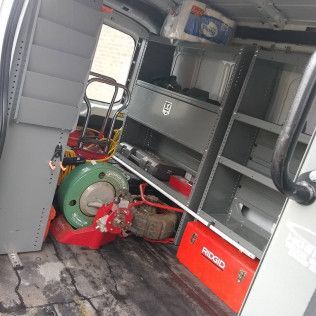 Interior of a service van. Shelves and tools visible. A plumbing snake and a Ridgid toolbox are present.