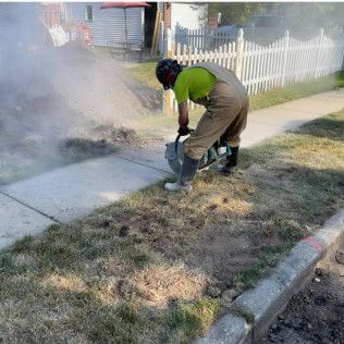 Person using a power tool to cut grass near a sidewalk; smoke rising.