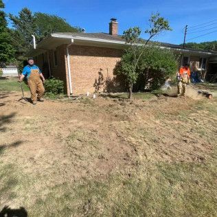Two workers digging in a yard next to a brick house. Sunny day.