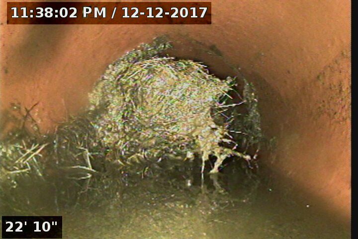 A camera view inside a pipe shows a large mass of tangled material and debris.