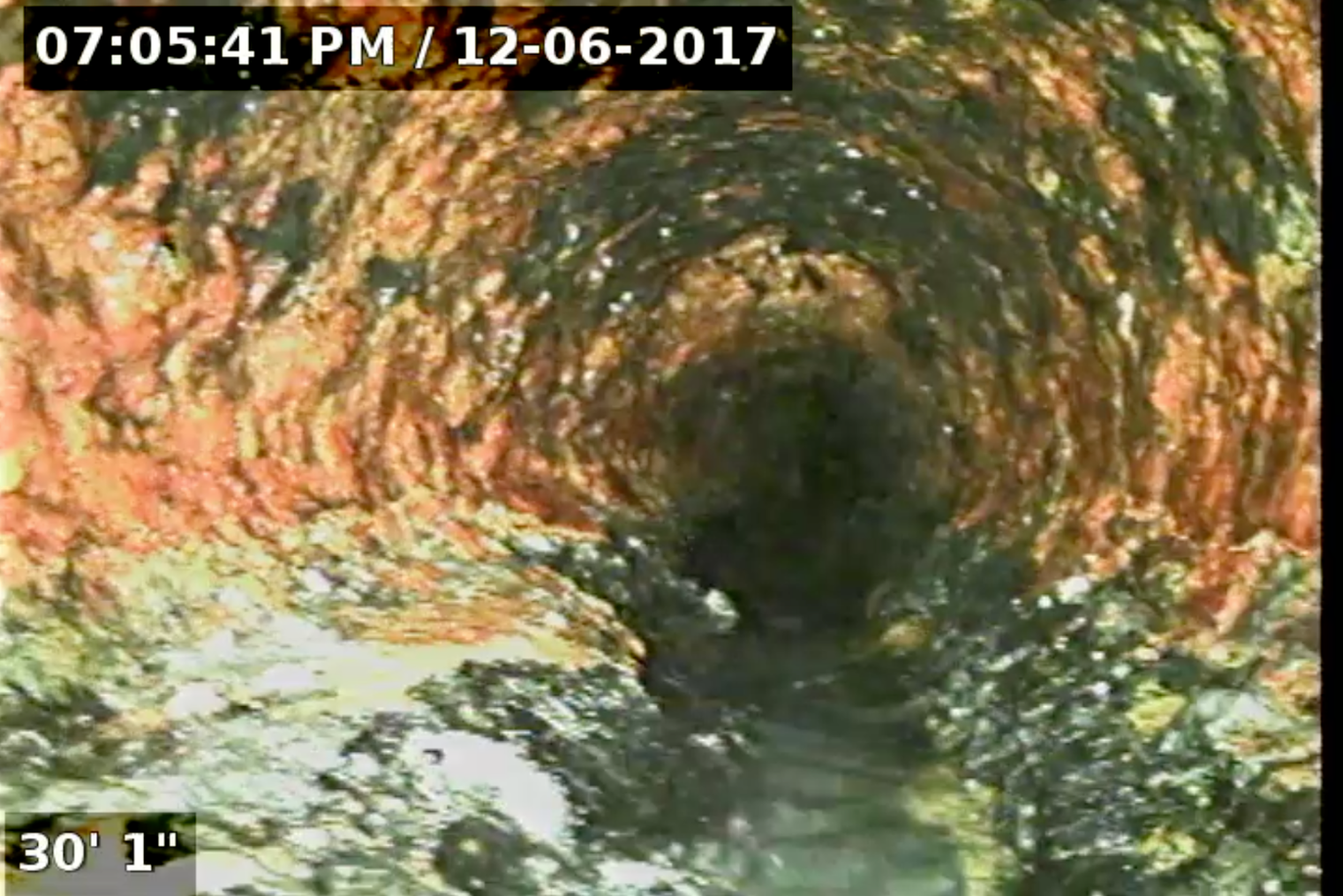 Interior view of a corroded pipe, with orange and dark-colored mineral buildup; timestamped 2017.