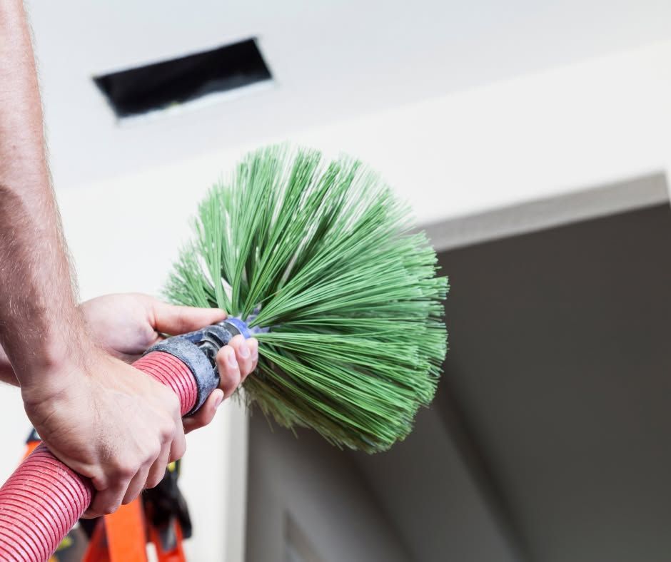 Person holding a green feather duster near a ceiling vent indoors