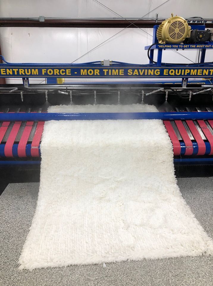 White carpet fabric on a textile machine with blue and red rollers in a factory.