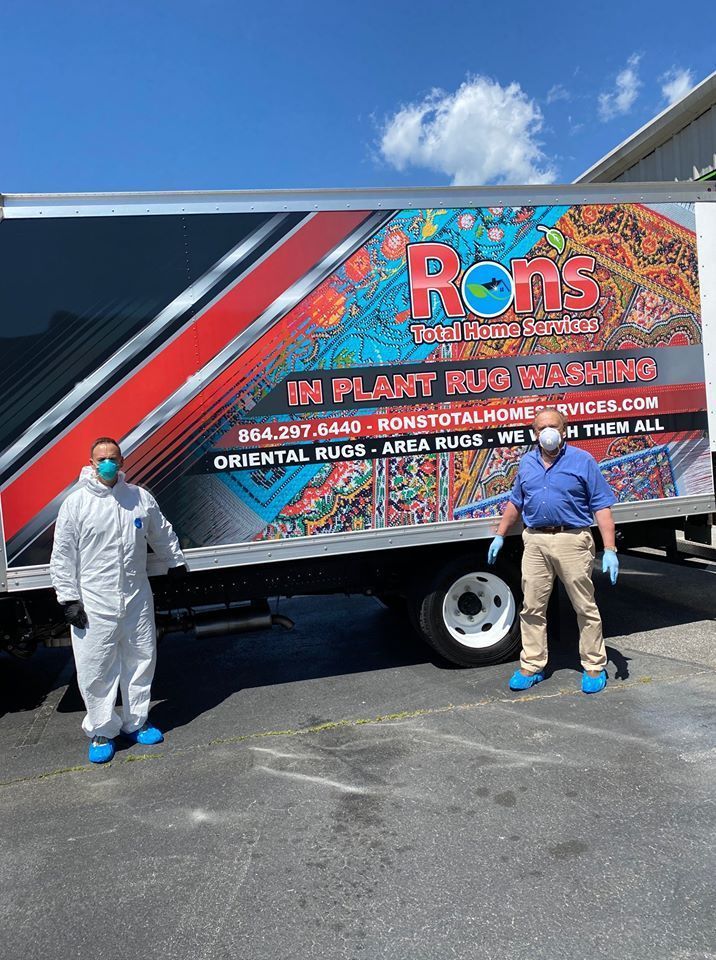 Two people in protective suits stand beside a Ron’s delivery truck with plant-mix branding in a parking lot.