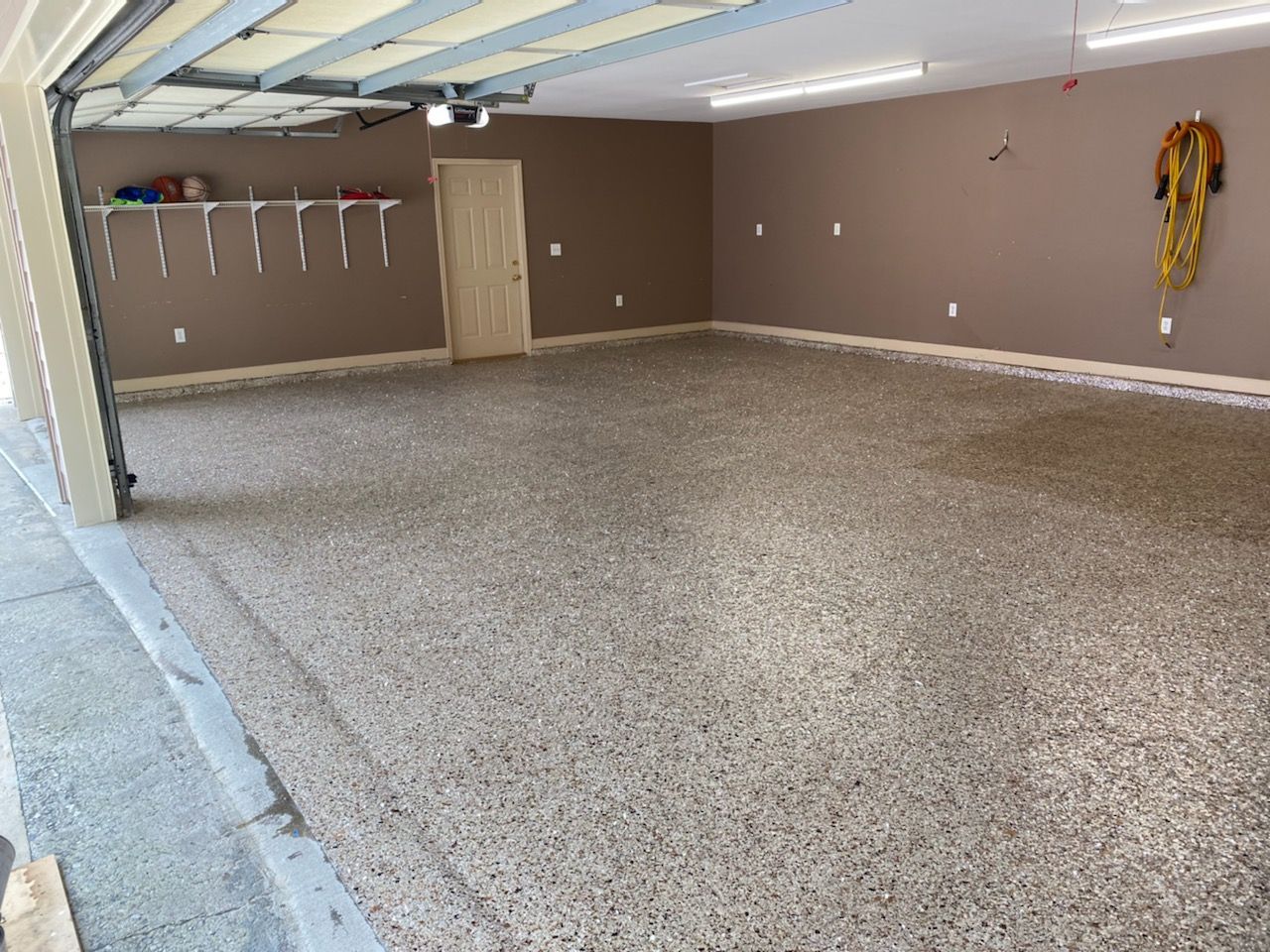 Empty garage interior with speckled floor, beige walls, and an open door to the left.