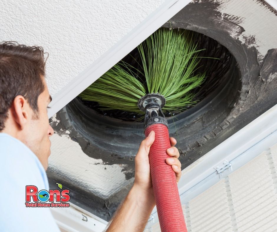 Technician cleaning a ceiling air vent with a red hose and brush