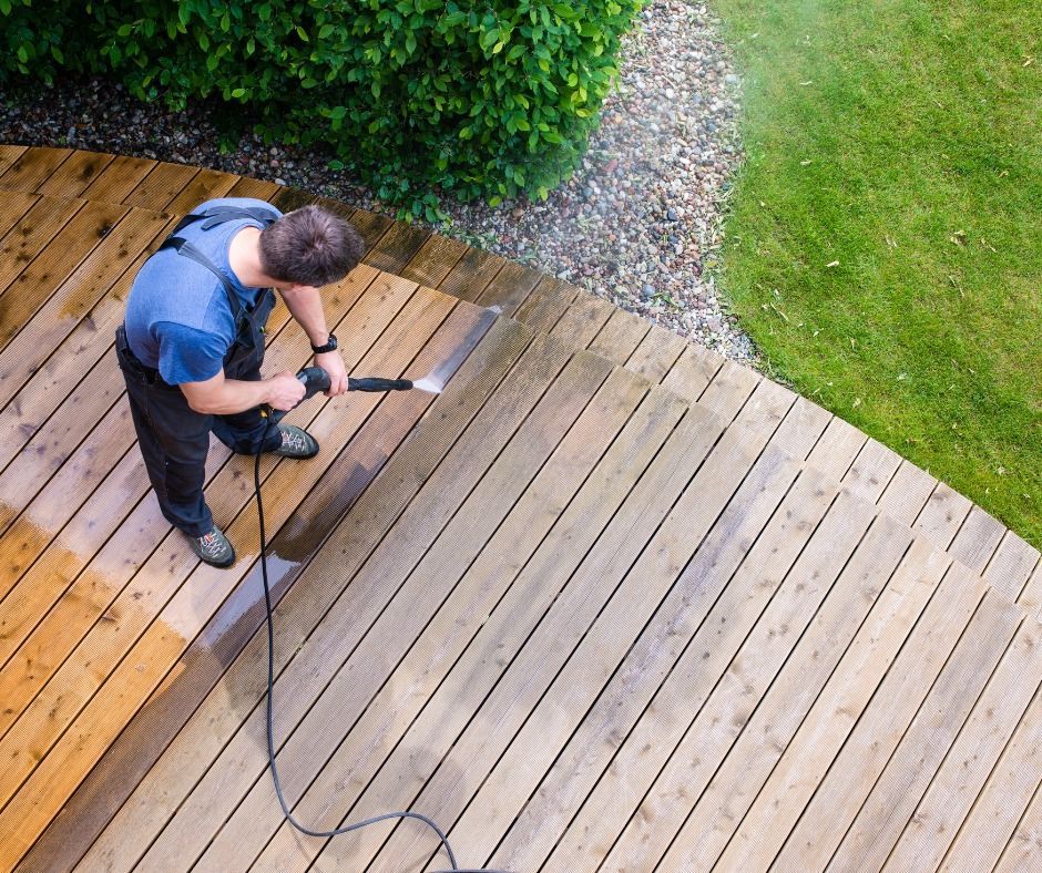 Person power-sanding a wooden deck beside grass and shrubs