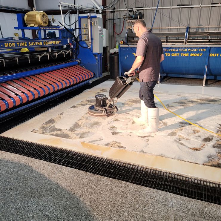 Worker using a floor grinder on a dusty industrial concrete slab next to blue machinery