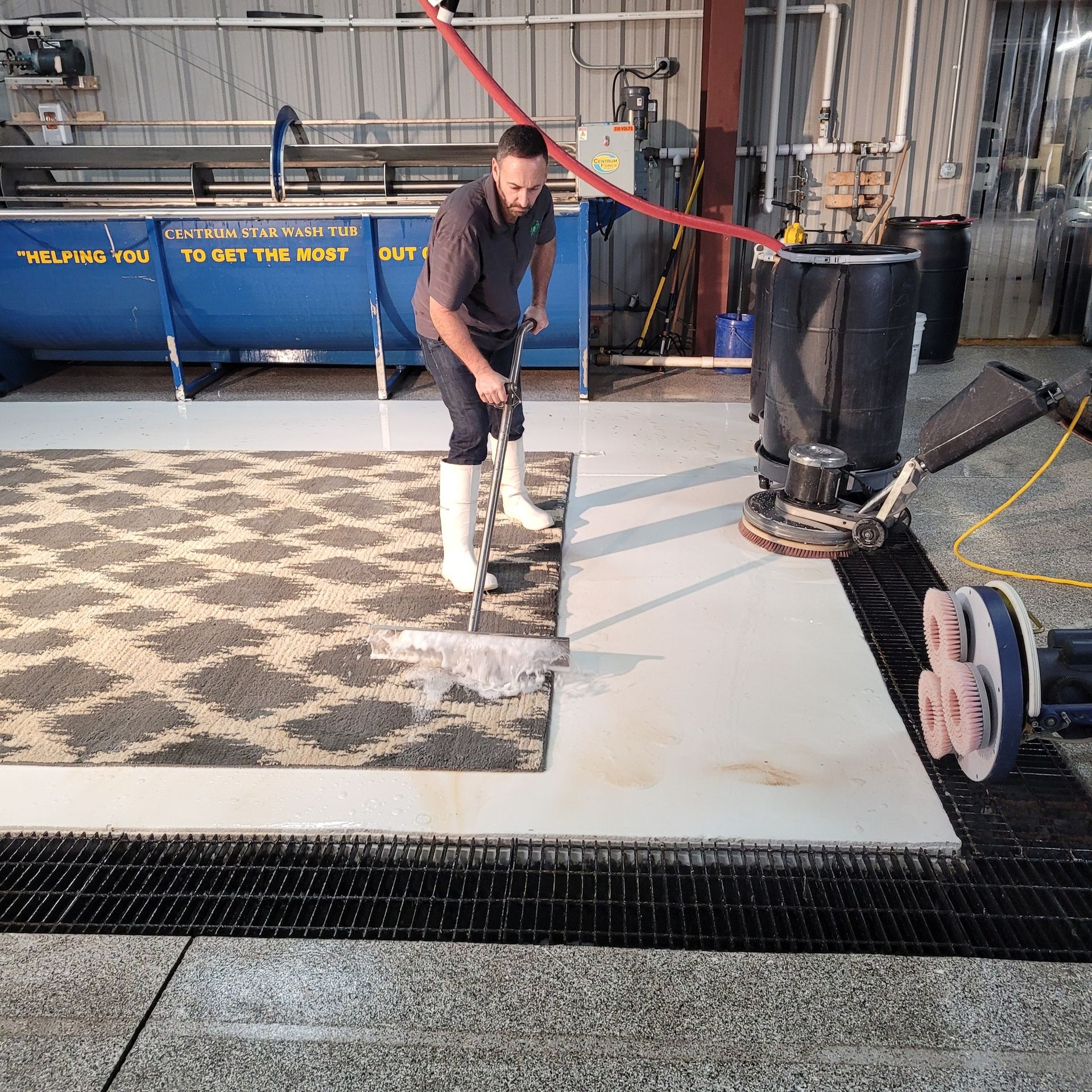 Worker scraping flooring in an industrial workshop beside machinery and bins.