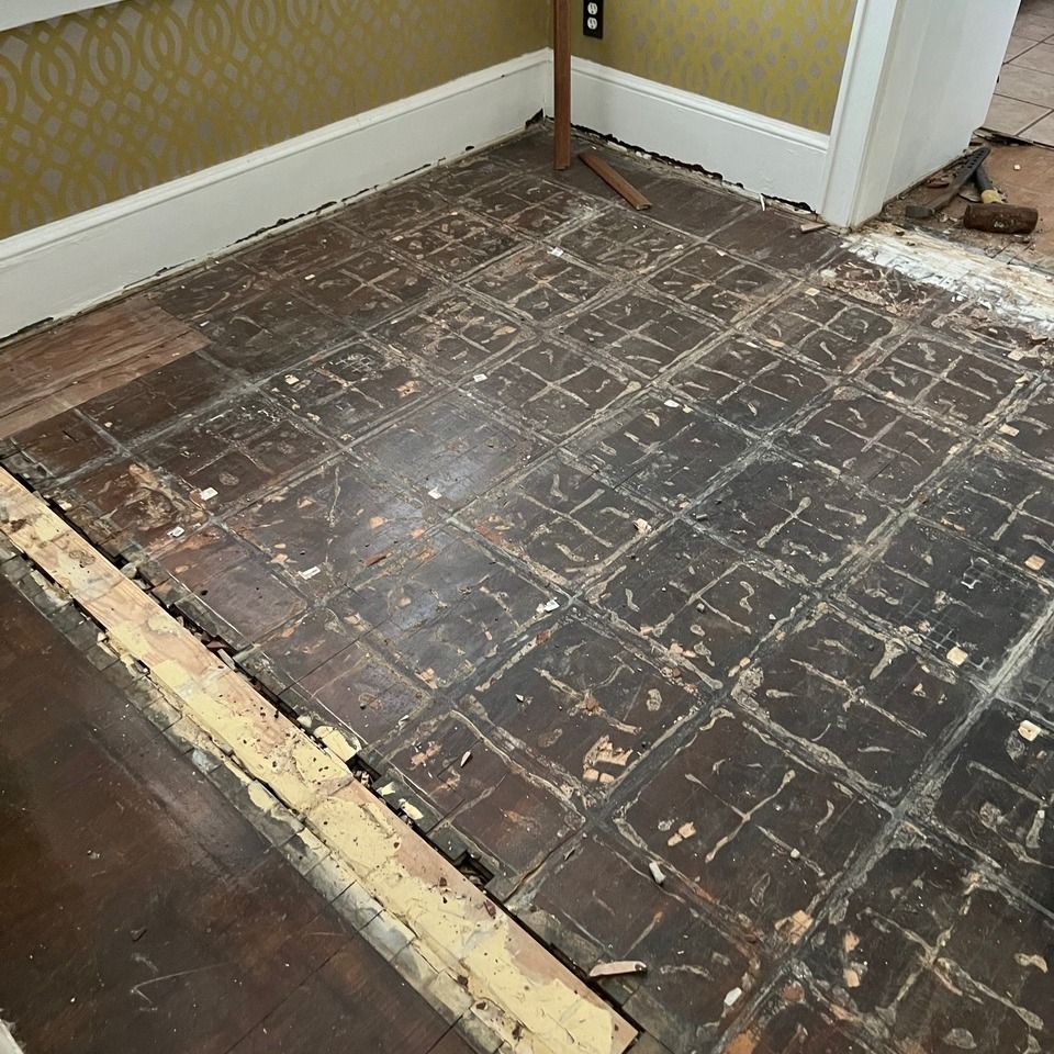 Damaged hardwood floor with sections removed, exposing subfloor in a room corner.