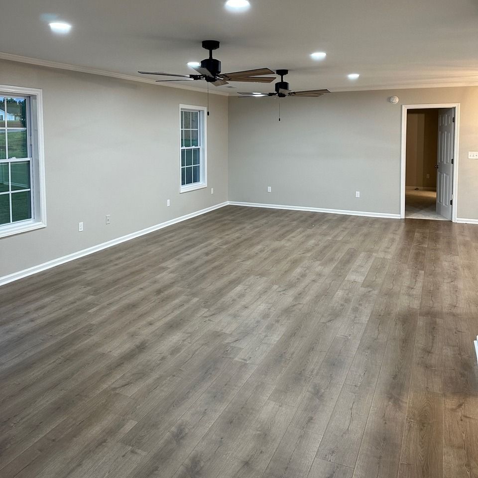 Empty living room with wood-look flooring, ceiling fan, and white walls with windows and doorway