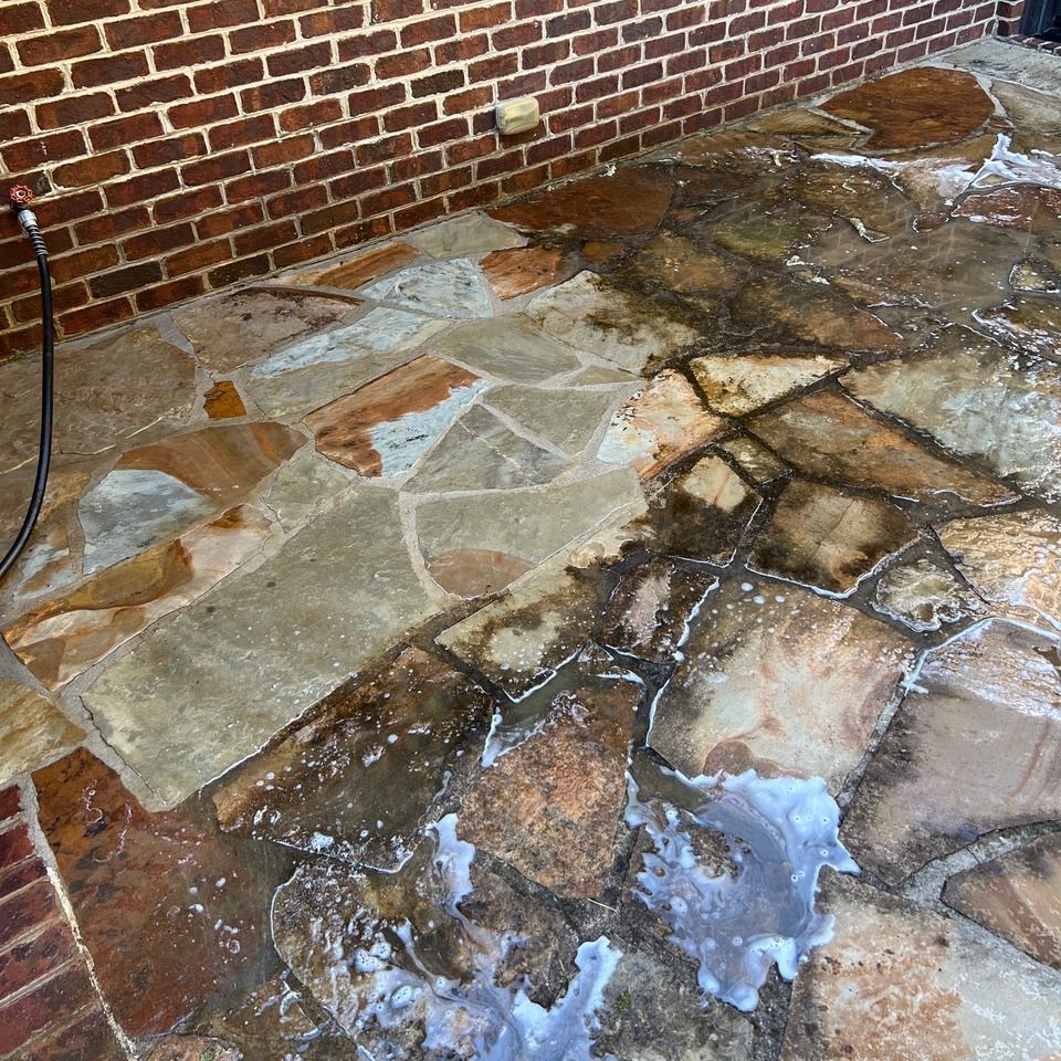 Wet stone patio beside a brick wall, with puddles reflecting light.