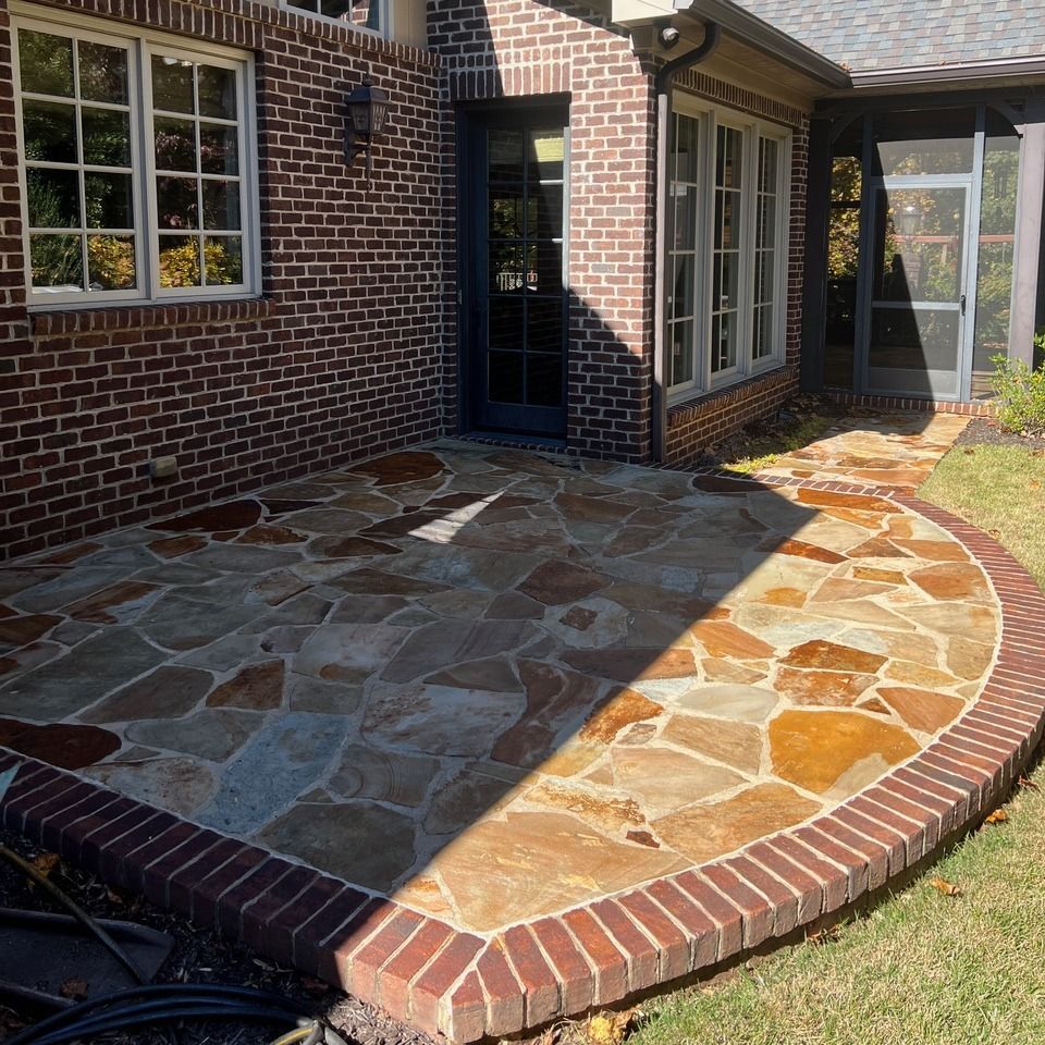 Brick house patio with irregular stone paving and a curved red brick border