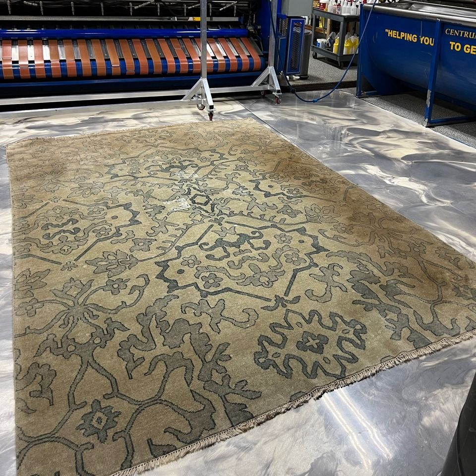 Beige patterned area rug laid on a shop floor, with rug-cleaning equipment in the background.