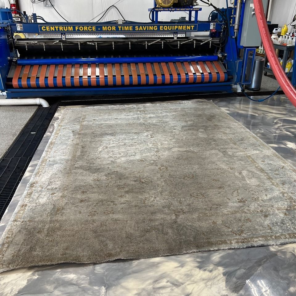Large industrial carpet-cleaning machine with a dirty gray rug on a wet concrete floor.