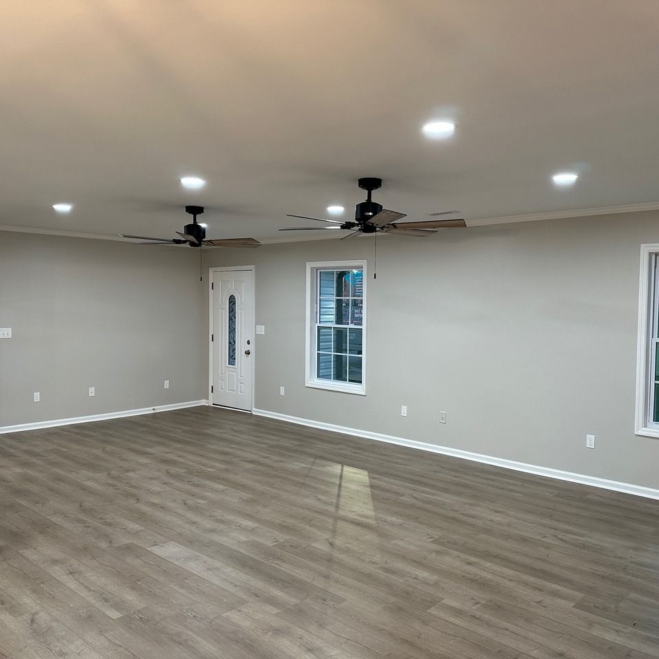 Empty living room with gray walls, wood-look flooring, recessed lights, ceiling fans, and white trim.