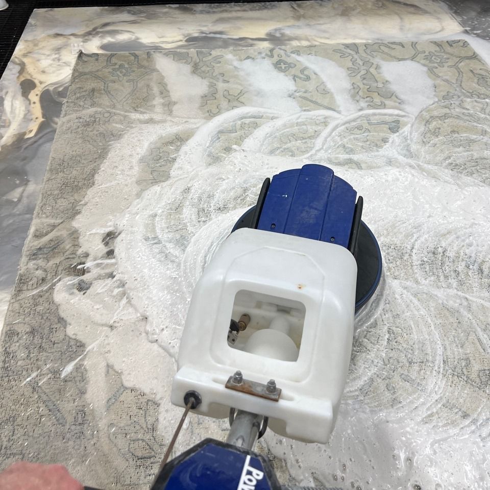 Blue-and-white floor scrubber cleaning a dusty concrete surface
