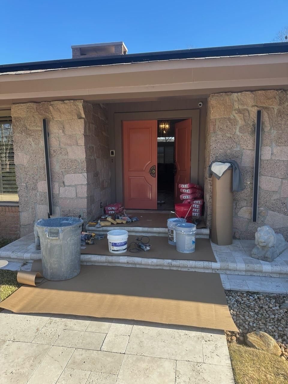 Front porch of a stone house with a red door, buckets, and supplies around the entrance.