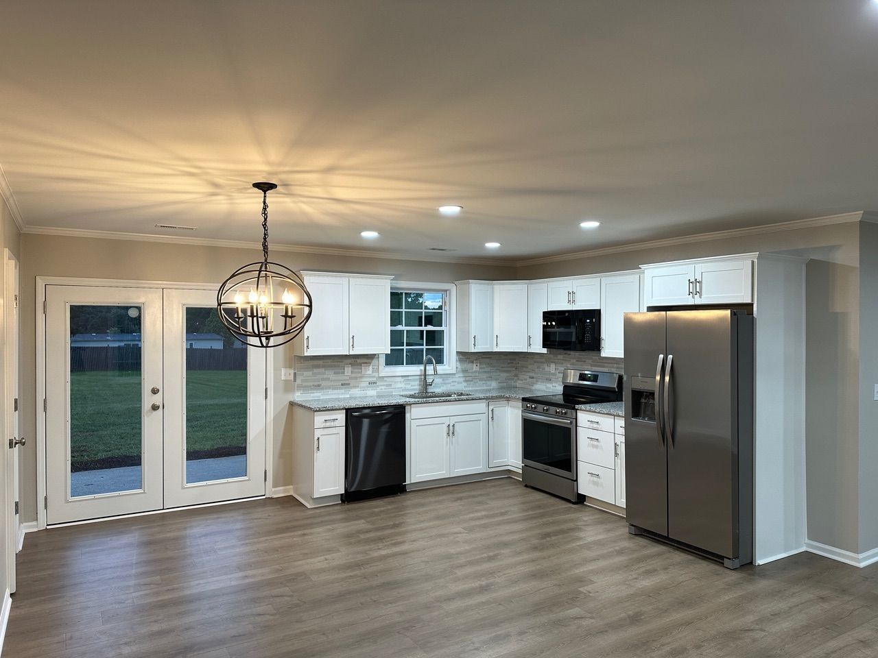 Bright modern kitchen with white cabinets, stainless appliances, pendant light, and wood-look flooring