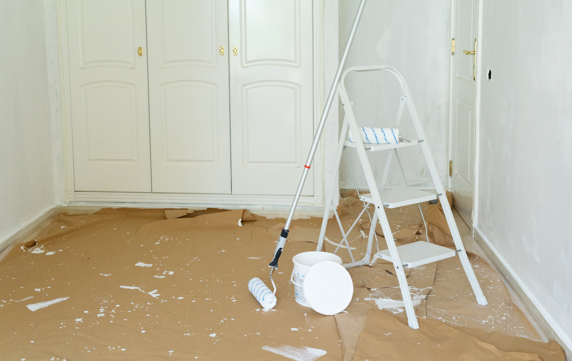 Paint-splattered room with drop cloth, ladder, and paint supplies during renovation