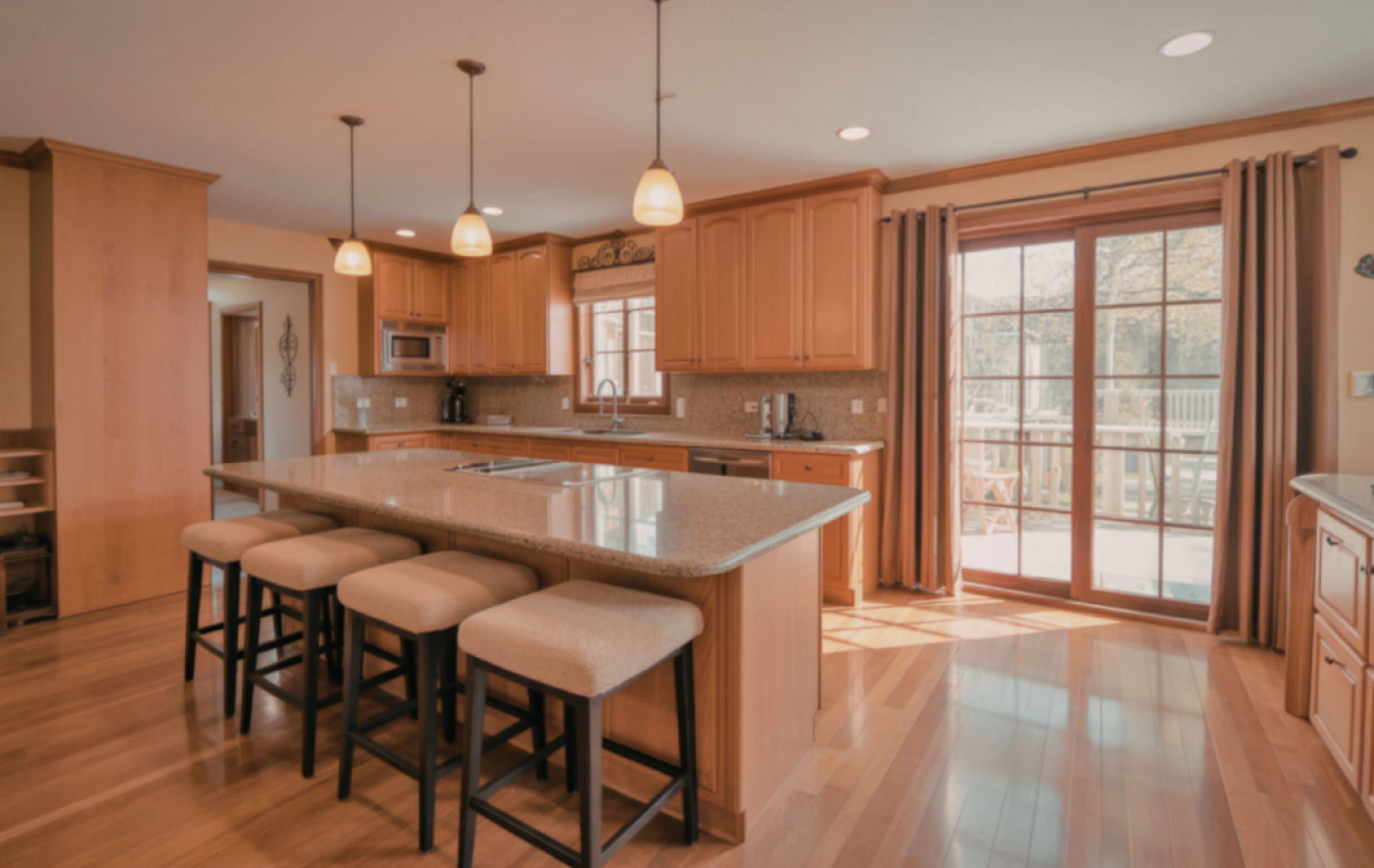 Bright kitchen with wood cabinets, granite island with stools, and sliding glass doors to a deck