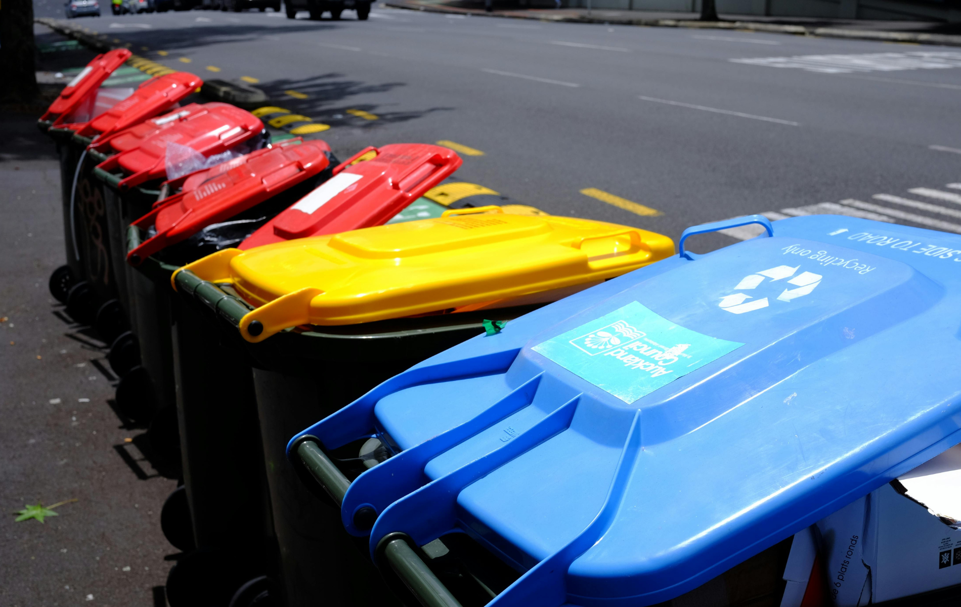 Row of colorful recycling bins lined up on a street, with a blue bin in the foreground