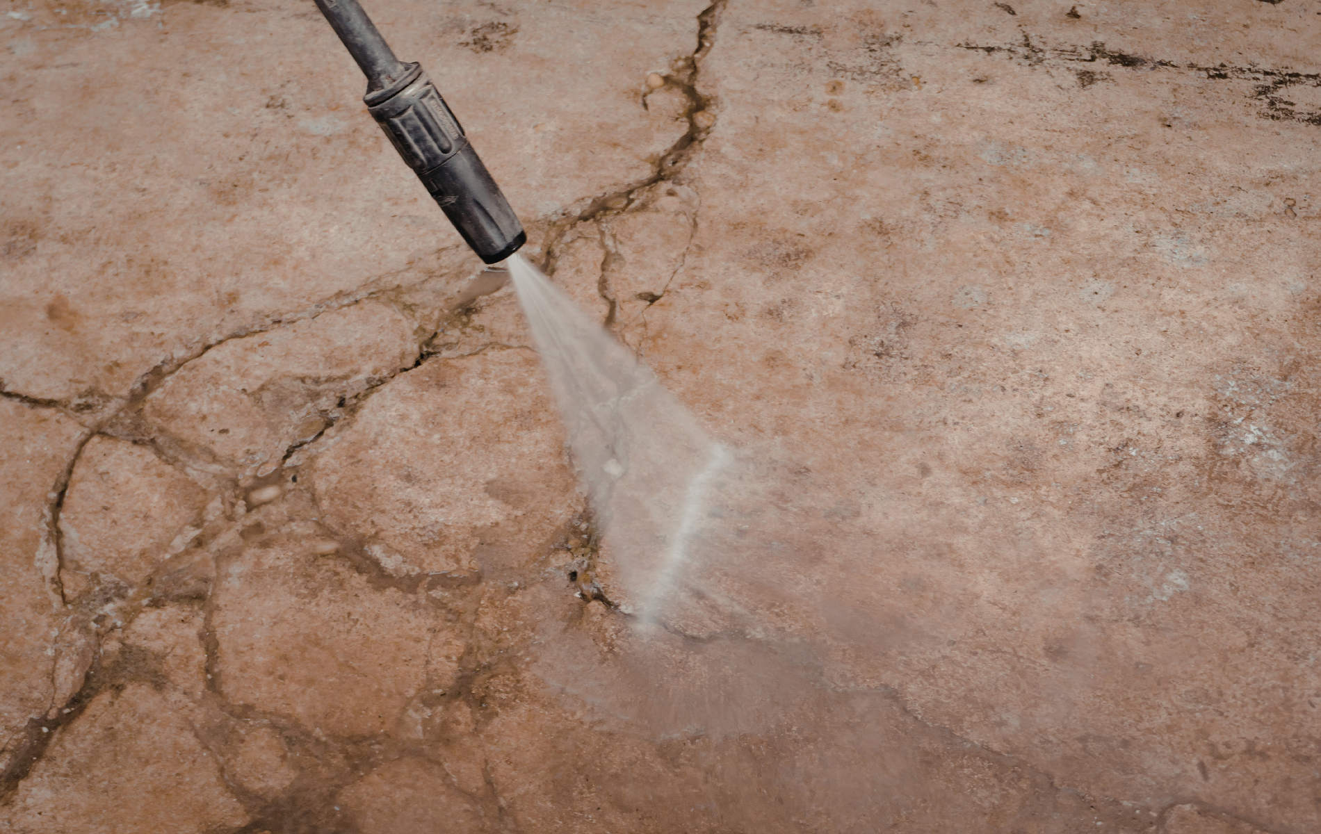 Pressure washer spraying water on cracked concrete ground