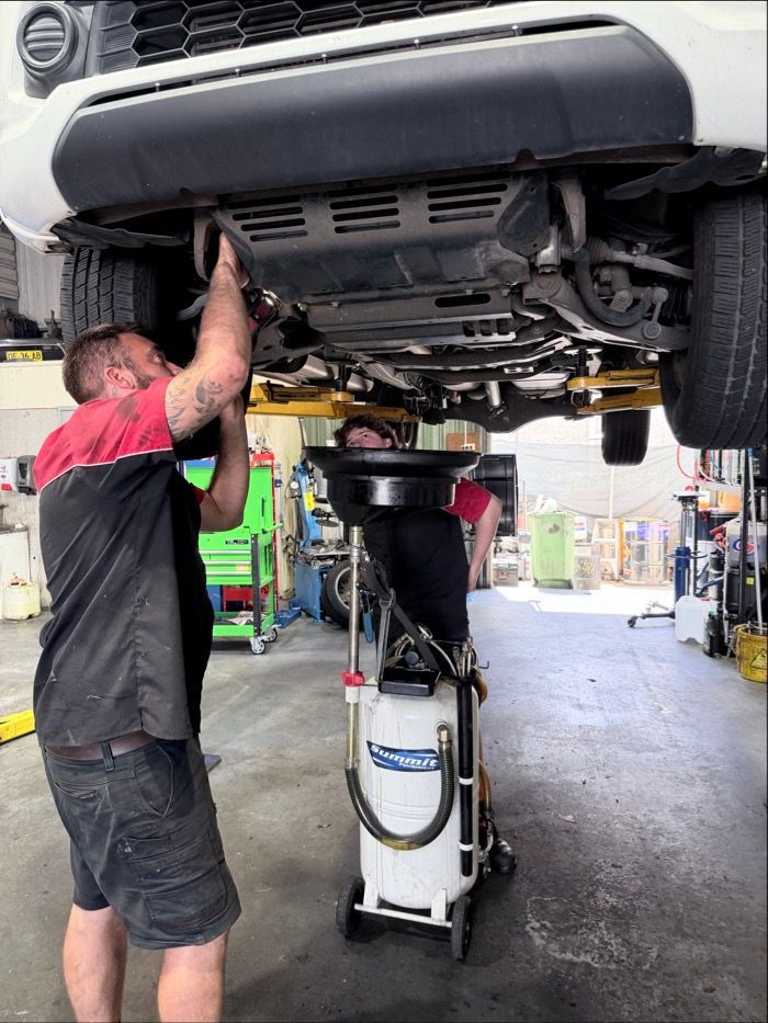 Two Mechanics Work Underneath a Raised Vehicle in A Garage — Morisset Automotive in Morisset, NSW