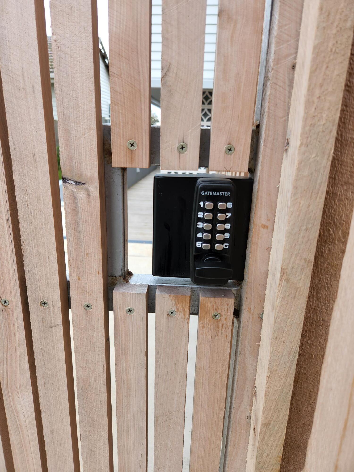 Black keypad on wooden gate with vertical slats.