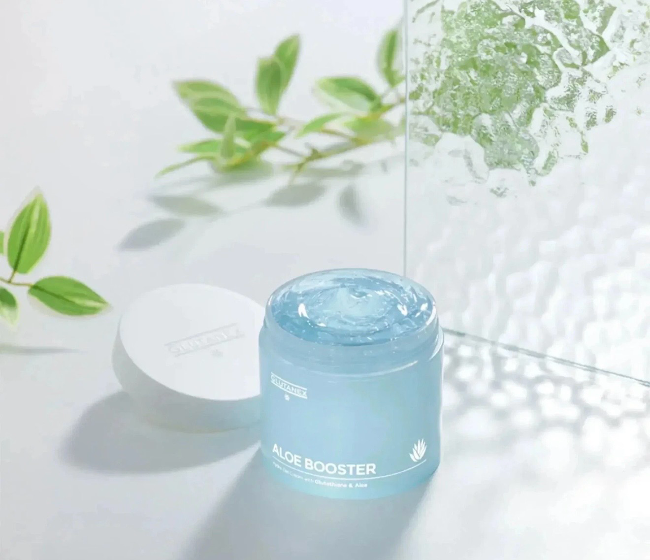 Blue cosmetic jar with white lid on a bright surface, surrounded by green leaves and water splash.