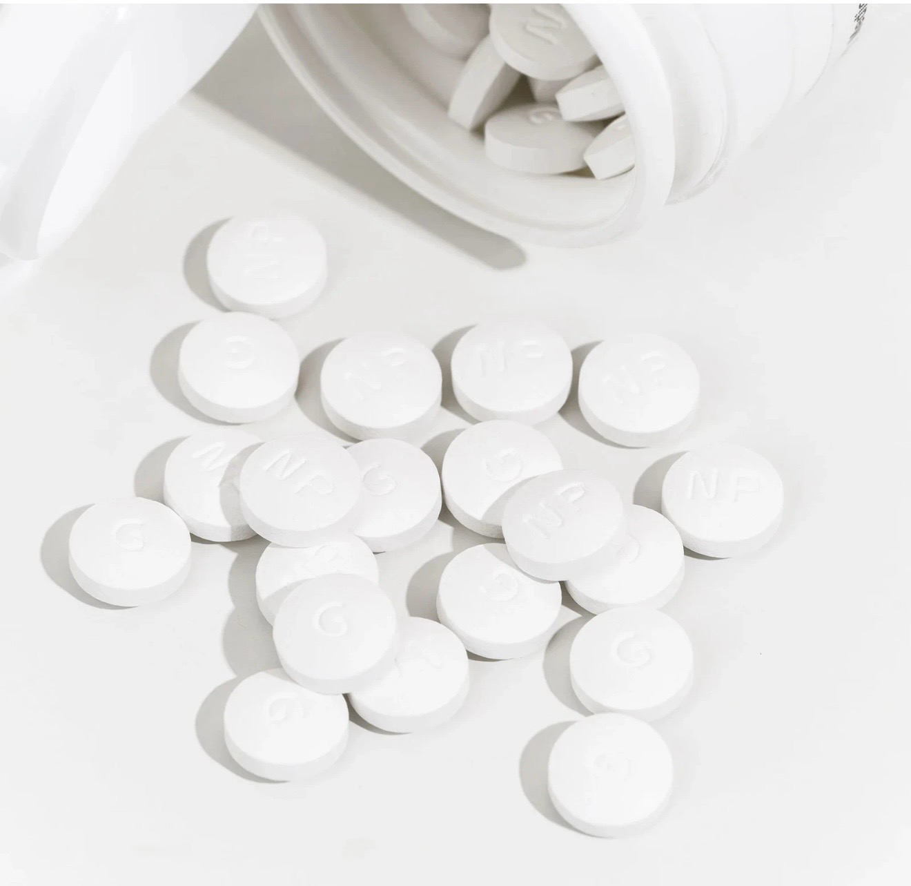 White round tablets spilled from an open white pill bottle on a white surface