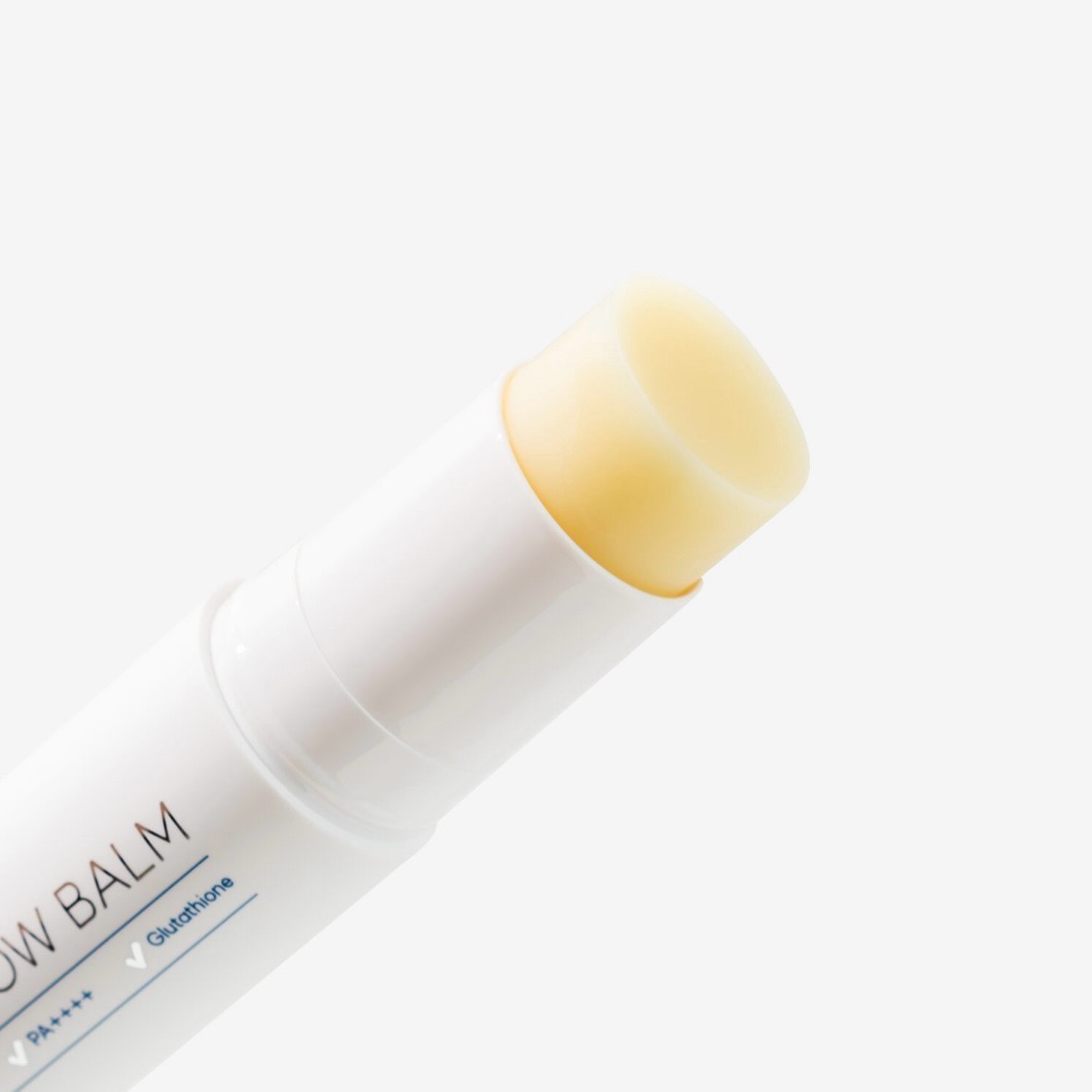 White lip balm stick with yellow balm, angled on a light background