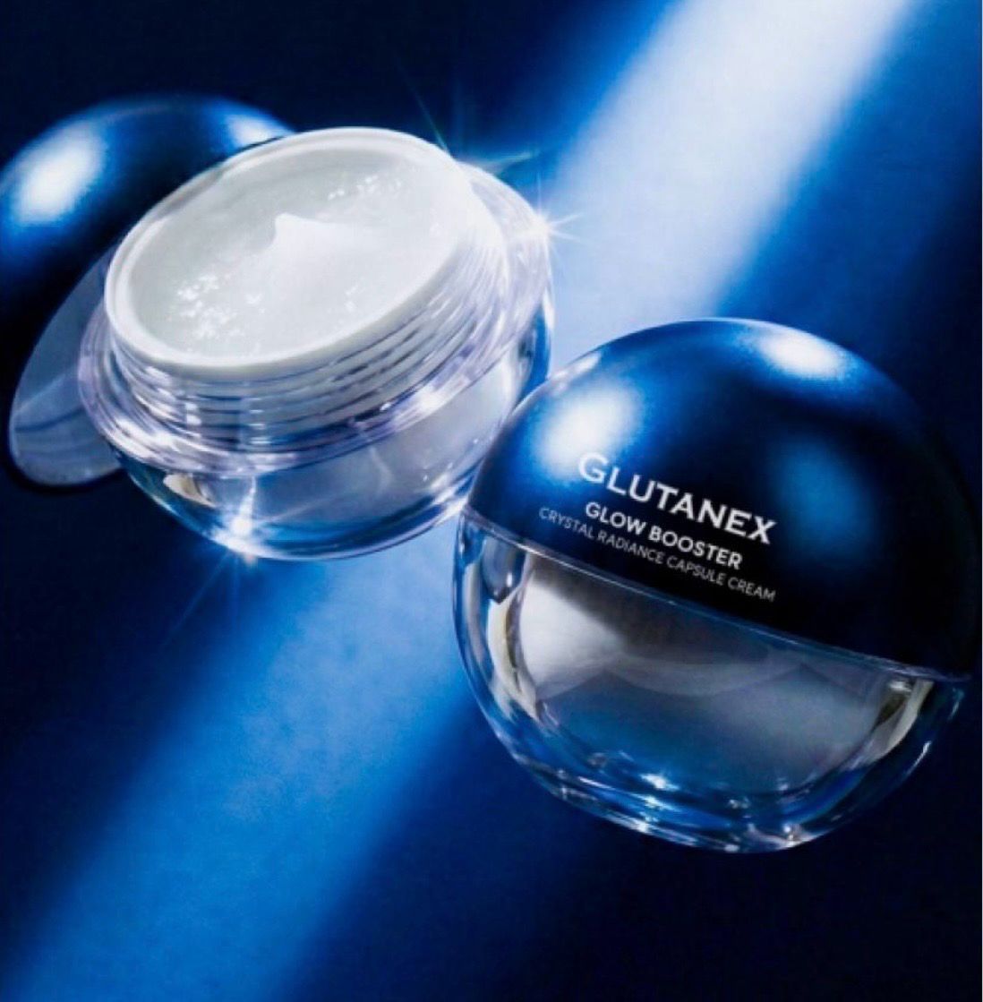 Two glossy blue skincare jars on a blue background, one open with white cream inside.