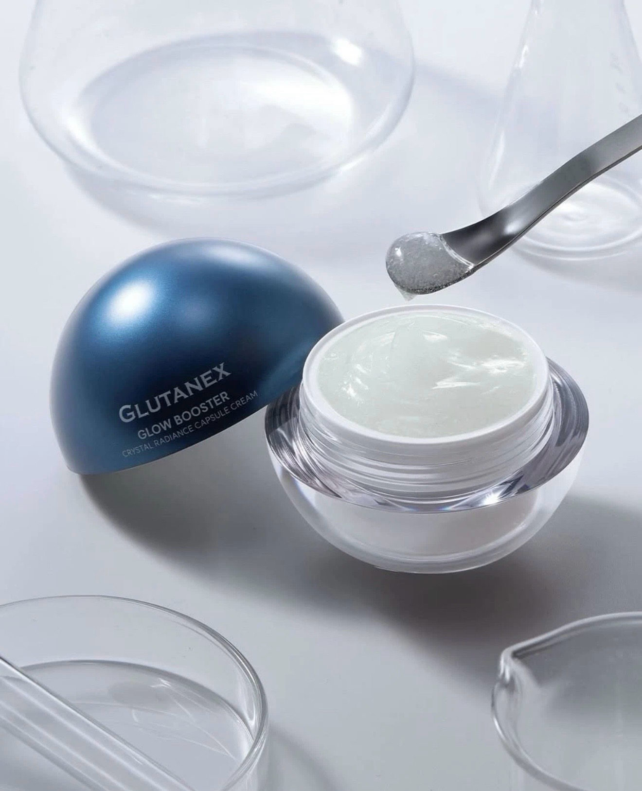 Open jar of white cream with dark blue lid and spoon on a light surface