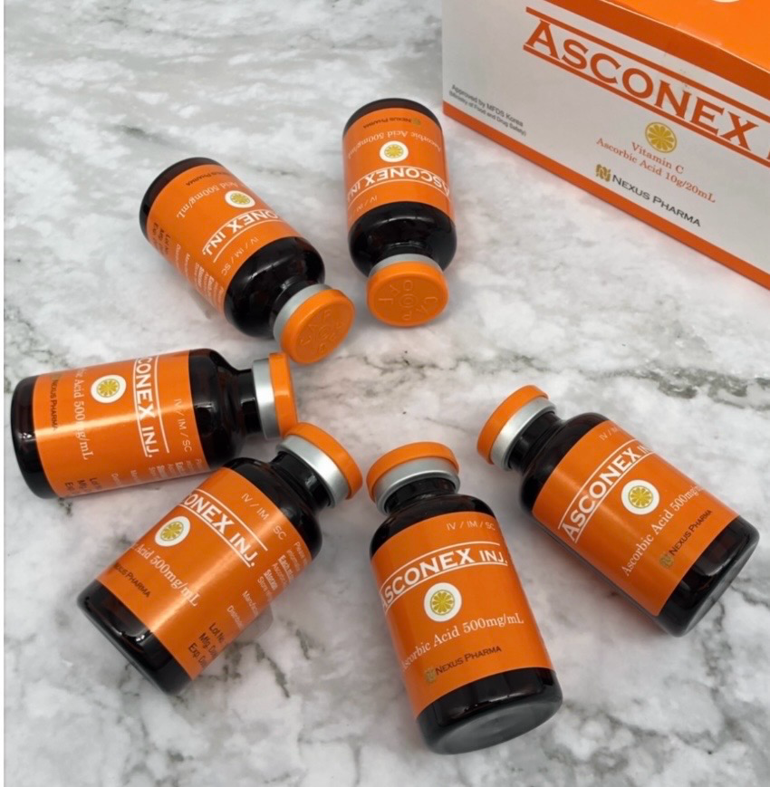 Several orange Asconex medicine bottles on a marble surface beside an Asconex box