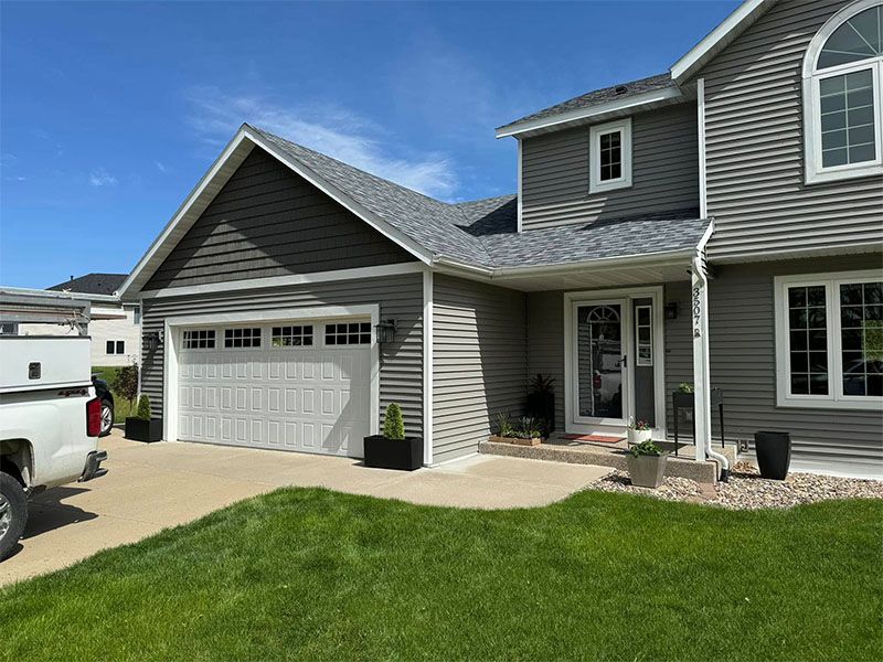 Gray house with a white garage door, front door, and windows, on a sunny day.