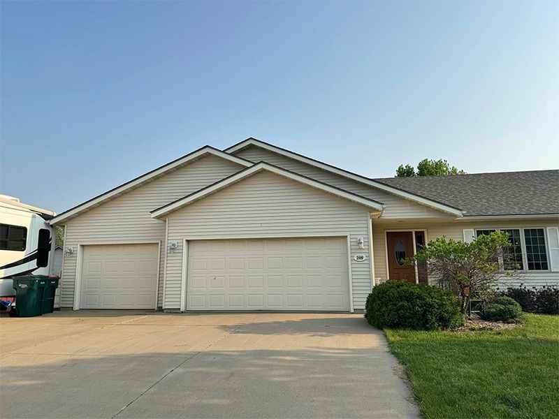 A tan house with a two-car garage, front door, and RV parked to the left.