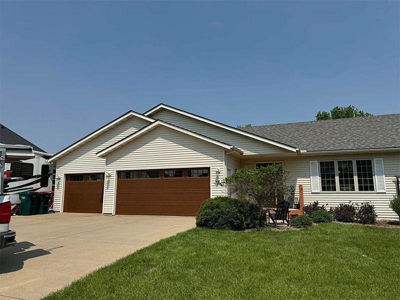Beige house with brown garage doors, green lawn, and blue sky.